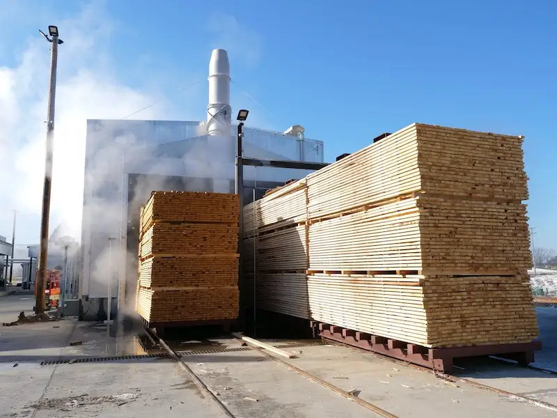 Steam venting from an open kiln with stickered packs standing on the rail carts outside it.