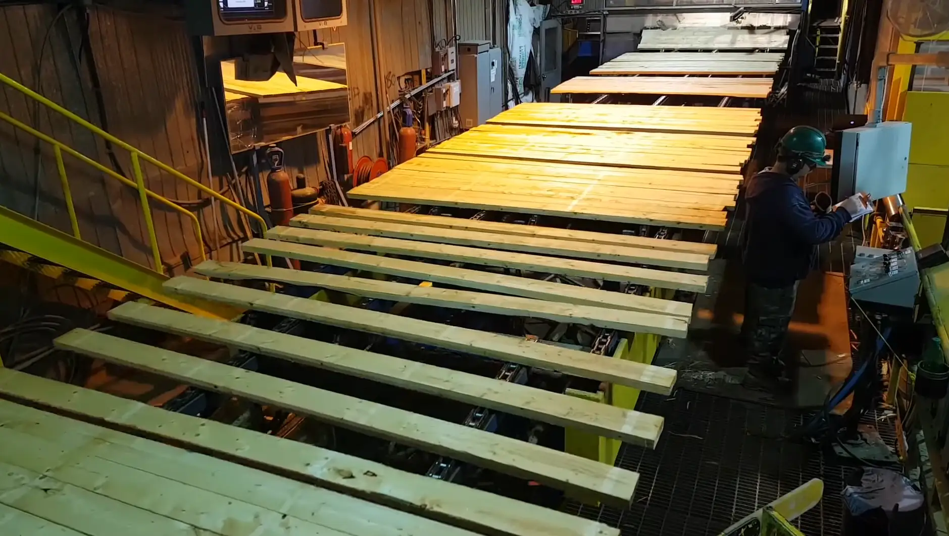 Surfaced boards spreading out across the transfer chains while an operator works the panel alongside them.