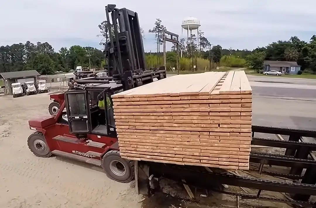 A forklift lifting a finished pack of rough lumber clear of the transfer chains in the yard.